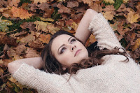 Eine junge Frau, die auf einem mit altem Laub bedeckten Waldboden liegt und nachdenklich in den Himmel sieht